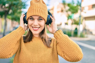 Genç sarışın kadın şehirde kulaklık takarak mutlu bir şekilde gülümsüyor..