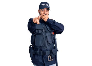 Polis üniforması giyen genç İspanyol adam sana gülüyor, eli ağzında kamerayı işaret ediyor, yüz ifadesi utanç verici. 