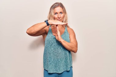 Orta yaşlı beyaz kadın spor kıyafetleri giyiyor. El kol hareketleri yapıyor, hayal kırıklığına uğramış ve ciddi bir yüz ifadesi takınıyor. 