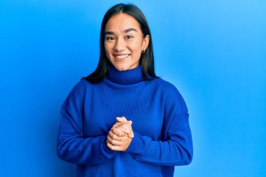 Genç Asyalı kadın, elleri çaprazlı, sıradan bir süveter giyiyor ve gülümsüyor. Rahat ve neşeli. Başarı ve iyimserlik 