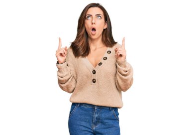 Kış süveteri giyen genç esmer kadın şaşkın şaşkın yukarı bakıyor, parmaklarıyla işaret ediyor ve kollarını kaldırıyordu.. 