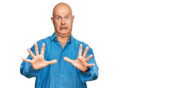 Orta yaşlı, kel, sıradan kıyafetler giyen, korku ifadesinden korkan ve dehşete düşmüş bir adam. El hareketlerini durdur, şok içinde bağır. panik konsepti. 