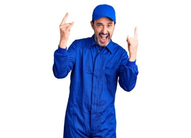 Orta yaşlı yakışıklı tamirci üniforması giyen çılgın bir ifadeyle bağıran elleri havada rock sembolü yapan bir adam. Müzik yıldızı. ağır müzik konsepti. 