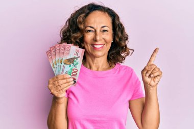 Orta yaşlı İspanyol kadın elinde 100 yeni Zelanda doları banknotuyla gülümsüyor. 