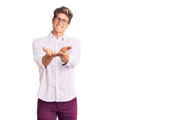 İş kıyafetleri ve gözlüklerle gülümseyen, el ele tutuşan genç yakışıklı bir adam el kol hareketi yapıyor. Bekleme ve koruma 