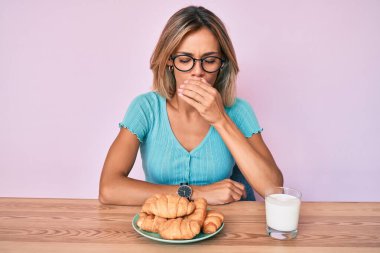 Kahvaltıda kruvasan yiyen güzel beyaz kadın kendini iyi hissetmiyor ve soğuk algınlığı veya bronşitin belirtisi olarak öksürüyor. sağlık hizmeti kavramı. 