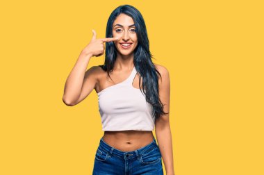 Güzel İspanyol kadın gündelik giysiler giyip el ve burnu işaret ediyor, neşeyle gülümsüyor. güzellik konsepti 