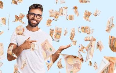 Gündelik kıyafetler giyen ve gözlüklü genç İspanyol adam kameraya hayret ediyor ve gülümsüyor..