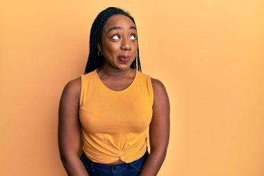 Genç Afrikalı Amerikalı kadın günlük kıyafetler giyiyor gülümsüyor, yan tarafa bakıyor ve düşünüyor.. 