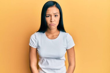 Gündelik beyaz tişört giyen güzel İspanyol kadın şüpheci ve gergin, sorun yüzünden surat asıyor. negatif kişi. 