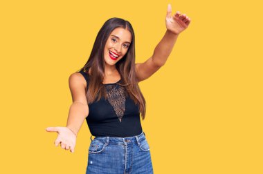 Gündelik giysiler giymiş genç İspanyol kadın kameraya bakıp sarılmak için kollarını açmış gülümsüyor. Mutluluğu kucaklayan neşeli bir ifade.. 