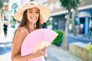Tatilde olan genç İspanyol kadın yaz stili giyiniyor. Şehrin sokaklarında el yelpazesi kullanıyor.