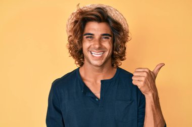 Yazlık şapkalı, gülümseyen, gülümseyen, gülümseyen ve başparmağıyla yan tarafı gösteren İspanyol genç adam.. 