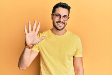 Gündelik kıyafetler giyen ve gözlük takan genç İspanyol adam beş numarayı gösterip işaret ederken kendinden emin ve mutlu gülümsüyor.. 