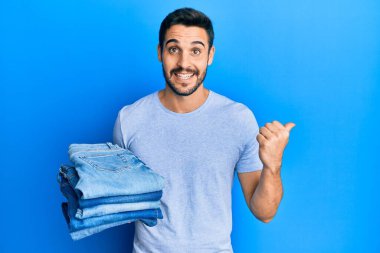 Bir yığın katlanmış kot pantolon tutan genç İspanyol adam başparmağını yukarı kaldırıyor ve ağzı açık gülümsüyor. 