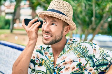 Beyaz tenli yakışıklı adam dışarıda mutlu bir şekilde gülümsüyor. Telefondaki sesli mesajı dinliyor.