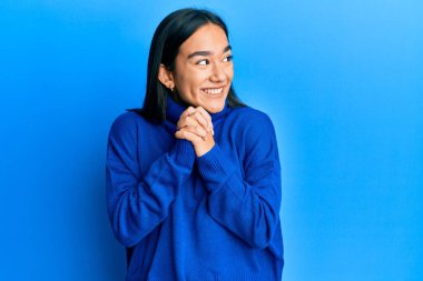 Kış süveteri giyen genç Asyalı kadın elleri çenesinde gergin ve heyecanlı bir şekilde yan tarafa bakıyor. 