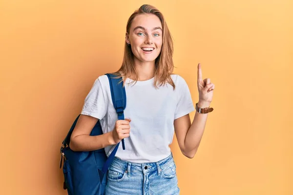 Beautiful blonde woman wearing student backpack smiling with an idea or question pointing finger with happy face, number one