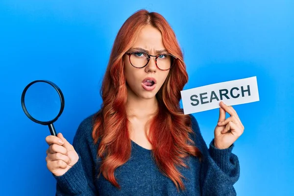 Young Redhead Woman Holding Magnifying Glass Search Word Shock Face — Stock Photo, Image