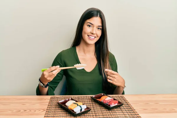 Joven Morena Comiendo Sushi Sentada Mesa Sonriendo Feliz Señalando Con — Foto de Stock