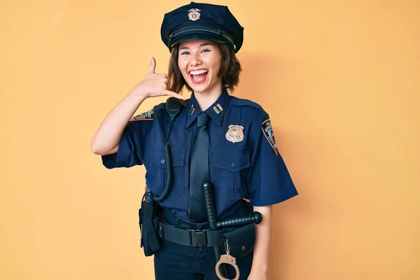 Young beautiful woman wearing police uniform smiling doing phone gesture with hand and fingers like talking on the telephone. communicating concepts.
