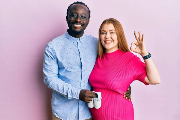 Jovem Casal Interracial Esperando Bebê Segurando Sapatos Fazendo Assinar Com — Fotografia de Stock