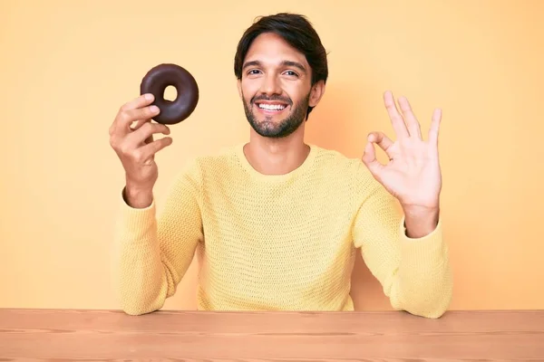 Bonito Homem Hispânico Segurando Donut Fazendo Sinal Com Dedos Sorrindo — Fotografia de Stock