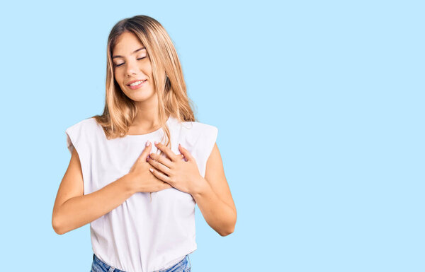 Beautiful caucasian woman with blonde hair wearing casual white tshirt smiling with hands on chest with closed eyes and grateful gesture on face. health concept. 