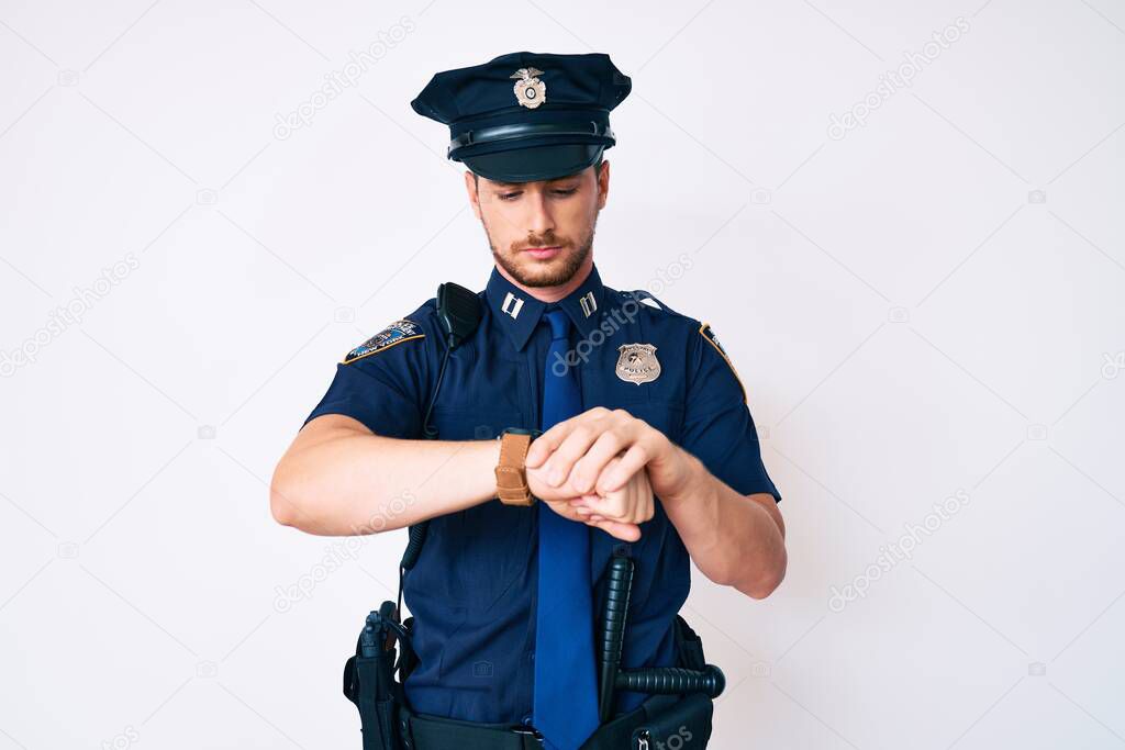 Young caucasian man wearing police uniform checking the time on wrist watch, relaxed and confident 