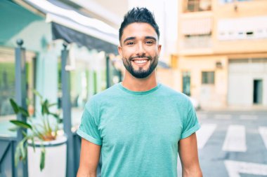 Genç Arap adam gülümsüyor, şehirde mutlu bir şekilde yürüyor..