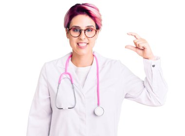 Pembe saçlı, doktor üniforması giyen, gülümseyen, kendine güvenen, el hareketleriyle hareket eden, parmaklarıyla işaret eden ve kameraya bakan genç, güzel bir kadın. ölçüm kavramı. 