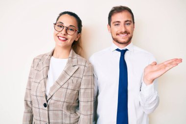 İş elbiseleri giymiş güzel bir çift neşeli bir şekilde sunum yapıyor ve avuç içiyle kameraya bakıyor.. 