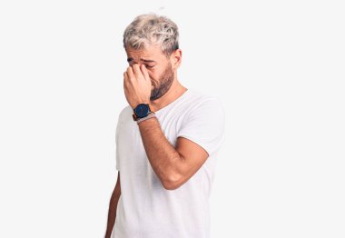 Genç, sarışın, gündelik tişört giyen, burnu ve gözleri ovuşturmaktan yorgun, yorgun ve baş ağrısı çeken bir adam. Stres ve hüsran kavramı. 