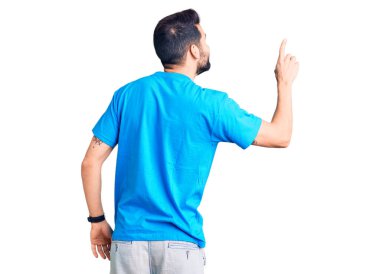 Sakallı, sıradan tişörtler giyen genç ve yakışıklı bir adam parmak eliyle öne doğru poz veriyor. 