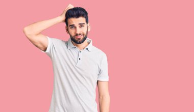 Sıradan polo kıyafetleri giyen sakallı yakışıklı genç bir adam soru sormayı merak ediyor. Şüpheyle kararsız, kafa kafaya düşünerek. Düşünceli kavram. 