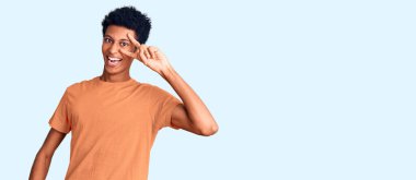 Genç Afro-Amerikan adam günlük kıyafetler giyiyor barış sembolü yapıyor. Yüzünde parmakları var, gülümsüyor ve zaferini gösteriyor. 