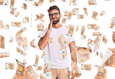 Günlük kıyafetler giyen ve gözlüklü genç bir İspanyol diş ağrısı ya da diş hastalığından dolayı ağızlarına acı dolu bir ifadeyle dokunuyor. dişçi