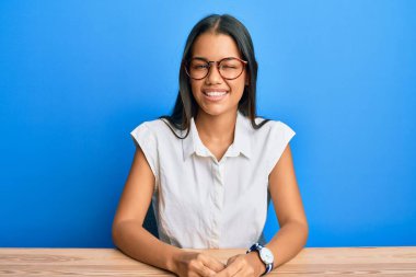 Güzel İspanyol kadın, gündelik giysiler içinde masada oturmuş kameraya seksi bir ifadeyle bakıyor, neşeli ve mutlu bir yüzle.. 