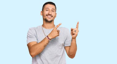 90 'ların tarzı dövmeleri olan yakışıklı bir adam gülümsüyor ve kameraya bakıyor iki eliyle ve parmaklarıyla kenarı işaret ediyor.. 