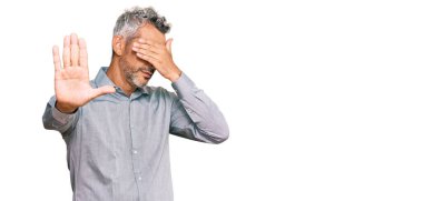 Orta yaşlı, gri saçlı, günlük kıyafetler giyen, elleriyle gözleri kapatan, üzgün ve korku ifadeli hareketler yapan bir adam. utangaç ve olumsuz kavram. 