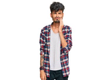 Günlük kıyafetler giyen genç İspanyol adam diş ağrısı ya da diş hastalığından dolayı acı dolu bir ifadeyle ağıza dokunuyor. dişçi 