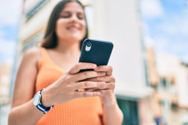 Ortadoğulu genç kız şehirde akıllı telefon kullanarak mutlu bir şekilde gülümsüyor..