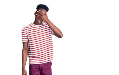 Genç, Afro-Amerikan bir adam günlük giysiler giymiş. Şoka girmiş, yüzünü ve gözlerini kapamış, utanmış bir ifadeyle parmaklarının arasından bakıyor.. 