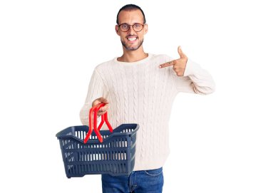 Süpermarket alışveriş sepetini tutan genç yakışıklı adam mutlu ve gururlu bir kendini işaret ediyor. 