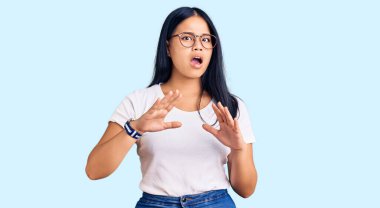 Genç, güzel Asyalı bir kız günlük kıyafetler ve gözlük takıyor korku ifadesinden korkuyor ve dehşete düşüyor. El hareketlerini bırak, şok içinde bağır. panik konsepti. 