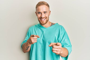 Gündelik giysiler giymiş genç beyaz bir adam mutlu ve komik yüzüyle kamerayı işaret ediyor. iyi enerji ve titreşimler. 