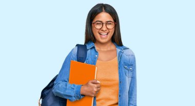 Öğrenci sırt çantası takan ve elinde kitaplarla kameraya bakan genç Latin kız. Seksi bir ifadeyle, neşeli ve mutlu bir yüzle.. 