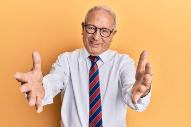 Beyaz üst düzey bir adam iş kıyafetleri içinde kameraya bakıp sarılmak için kollarını açmış gülümsüyor. Mutluluğu kucaklayan neşeli bir ifade.. 