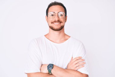 Sıradan kıyafetler giyen, gözlüklü mutlu yüzlü, kollarını kavuşturup kameraya bakan genç yakışıklı bir adam. pozitif kişi. 