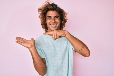 Gündelik kıyafetler giyen genç İspanyol adam kameraya hayret ediyor ve gülümsüyor.. 